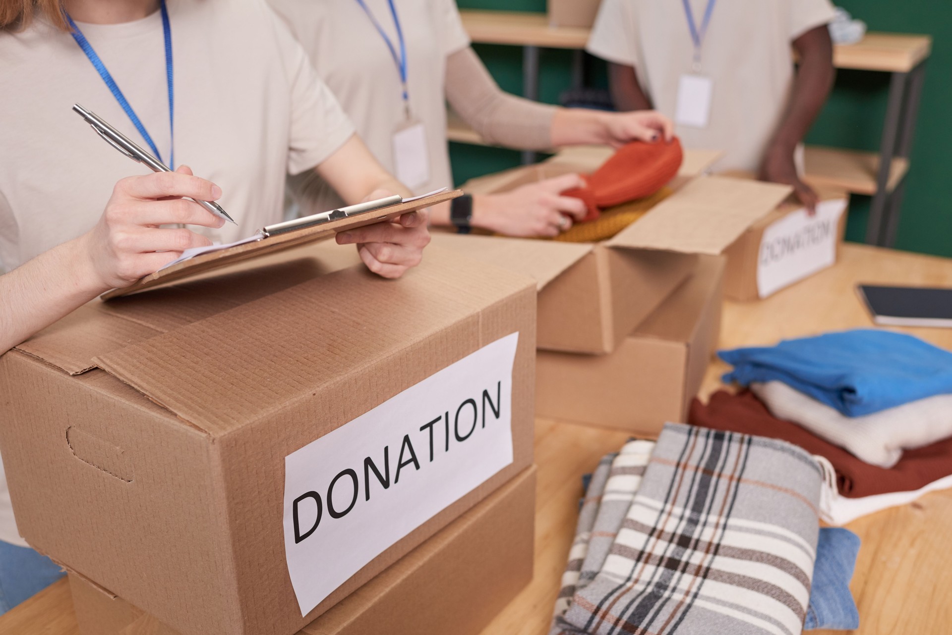 Group of unrecognizable young people volunteering in clothes charity checking and sorting out items